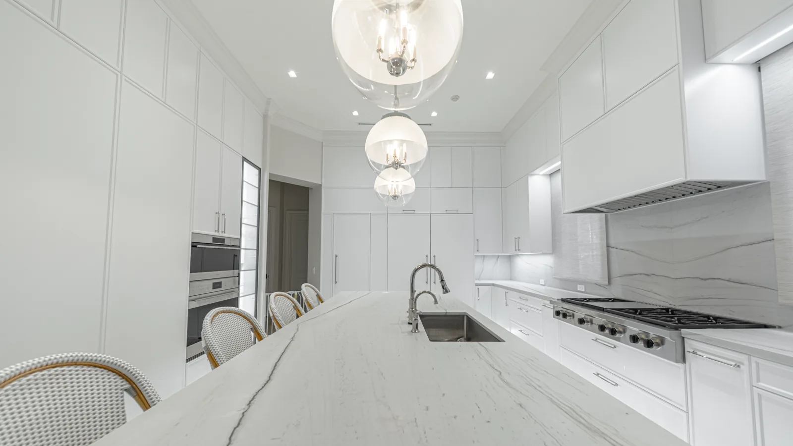 A finished designer kitchen with a marble island, glass pendants and a stainless range